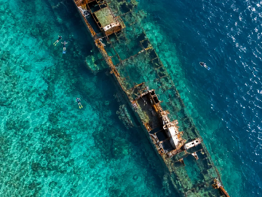Aerial view of a rusted shipwreck lying just below turquoise water